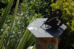 A sundial in the shape of a Butterfly, sat in amongst some shrubbery